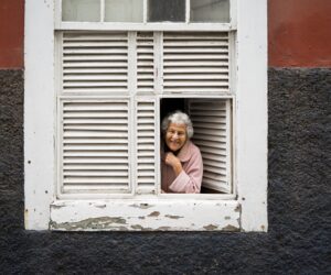 Smiling older woman leaning on an open window sill.