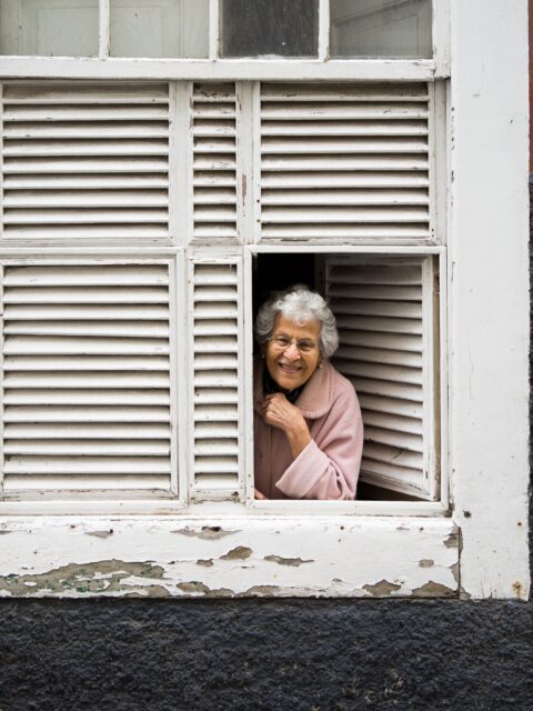 Smiling older woman leaning on an open window sill.