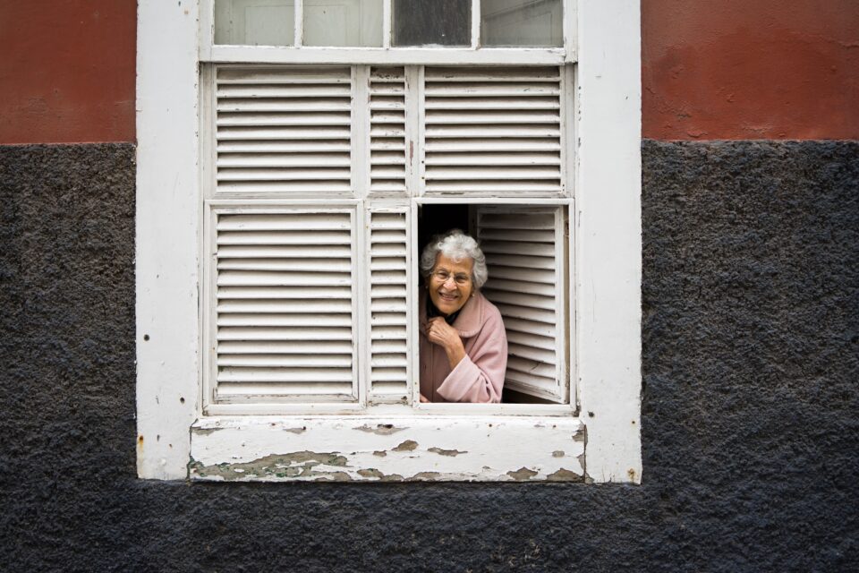 Smiling older woman leaning on an open window sill.