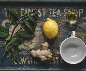 Ginger, lemon, mint, and a white cup arranged on a weathered wooden tray.